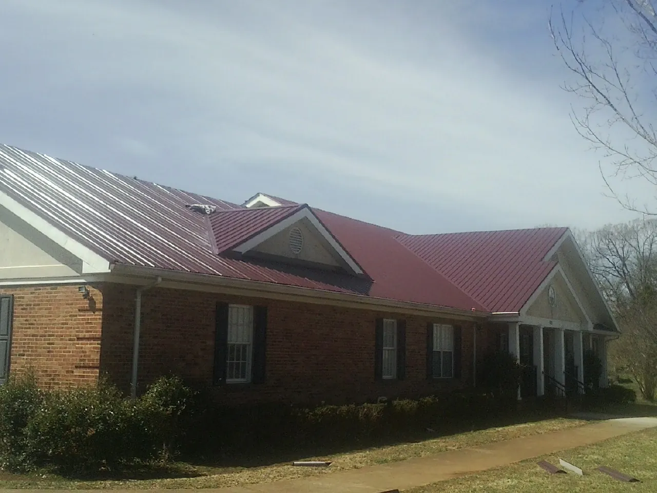 Red metal roof with gabled entries on a long brick building, from a Hail Damage Roof Repair job in Provo